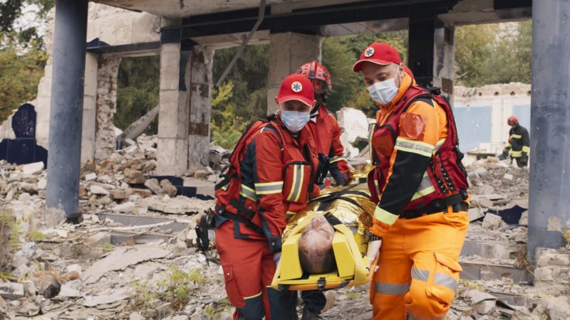 Photo of paramedics carrying a person on a stretcher surrounded by debris